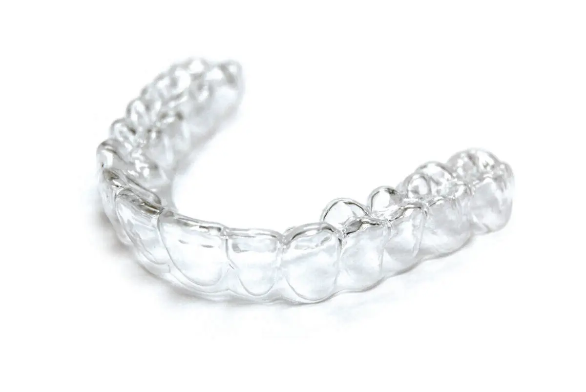 A clear aligner tray lit against a dark background