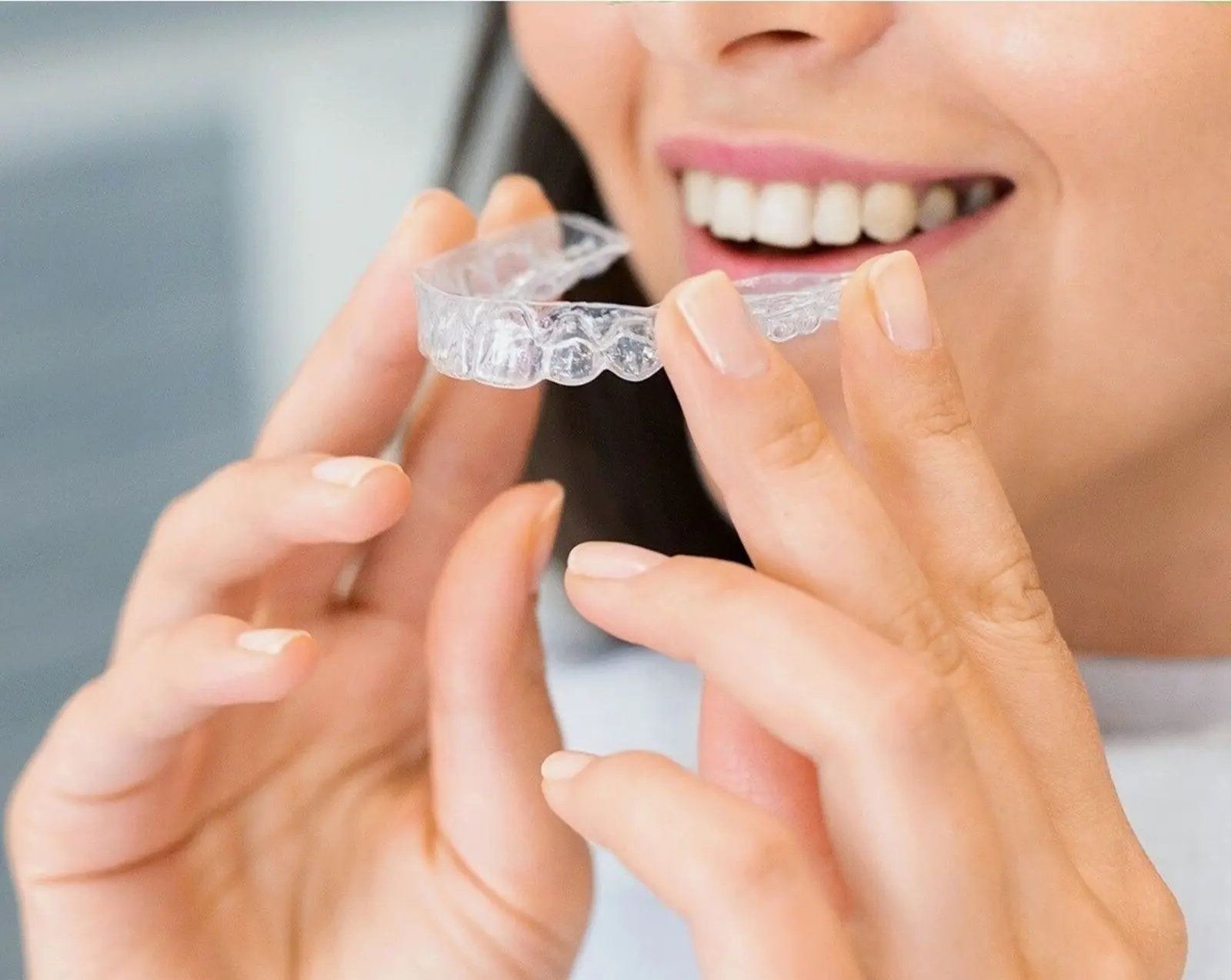 Woman smiling as she holds a clear dental aligner tray near her teeth