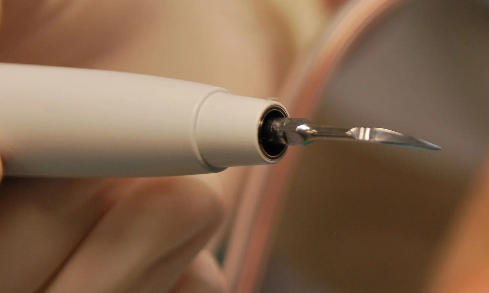 Gloved hand holding an ultrasonic scaler handpiece with a thin curved metal tip