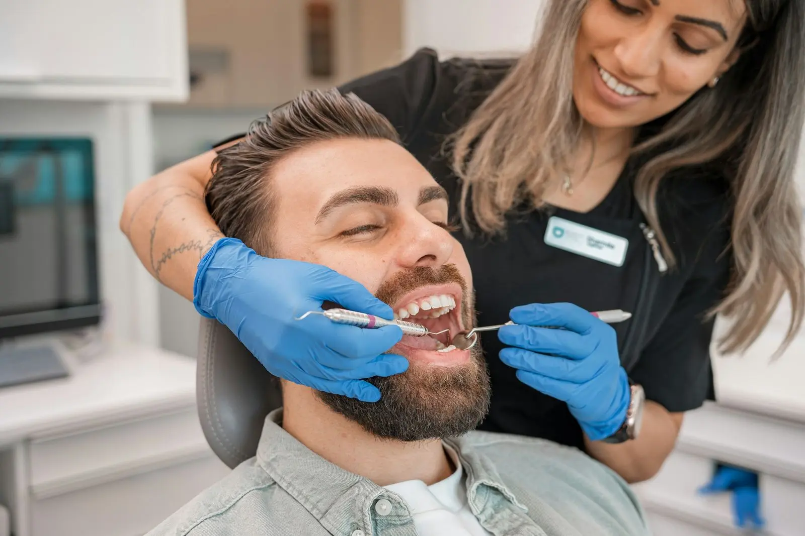 Dental hygienist checking a smiling patient's teeth with a mirror and probe