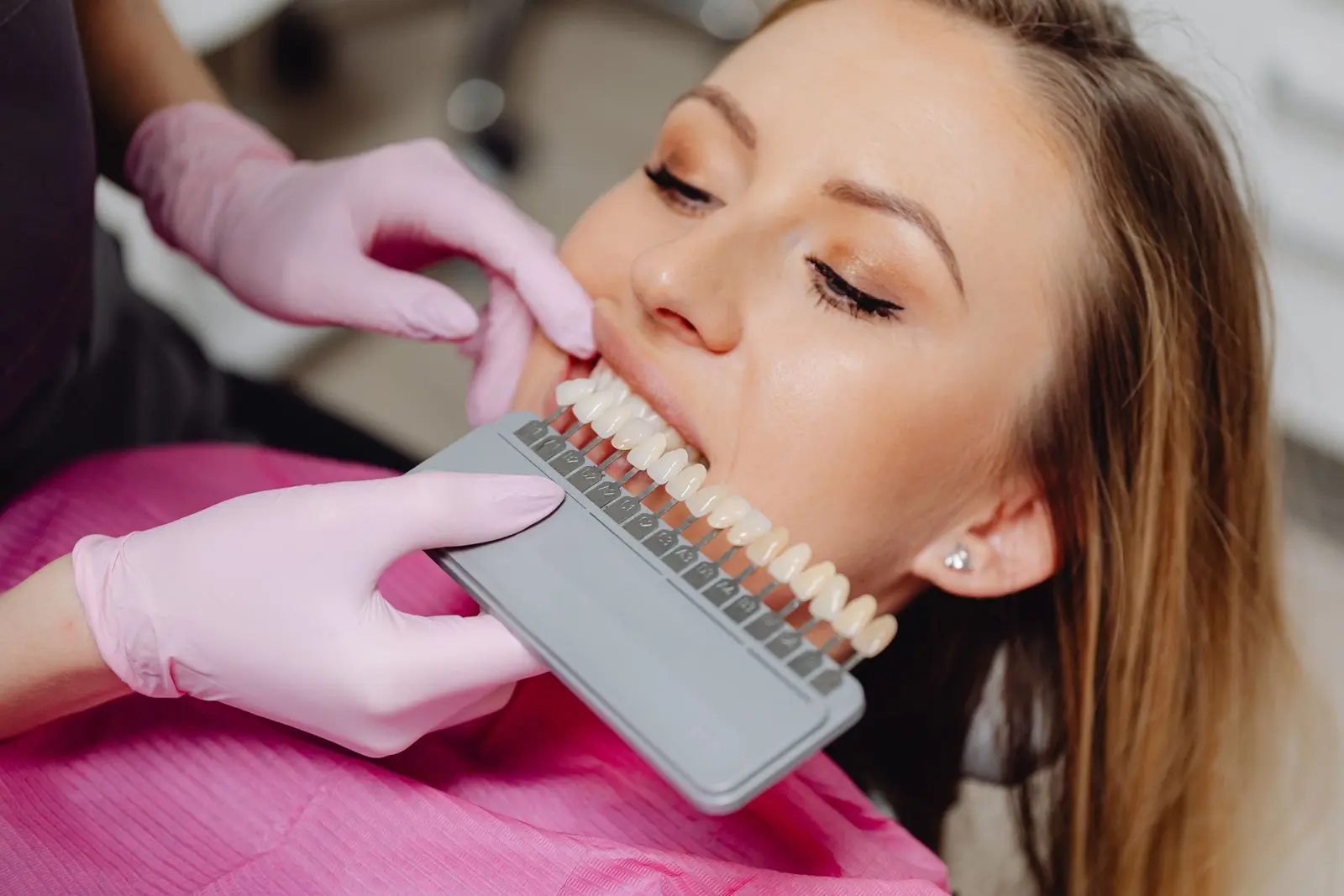 Dentist holding a tooth shade guide against a smiling patient's teeth